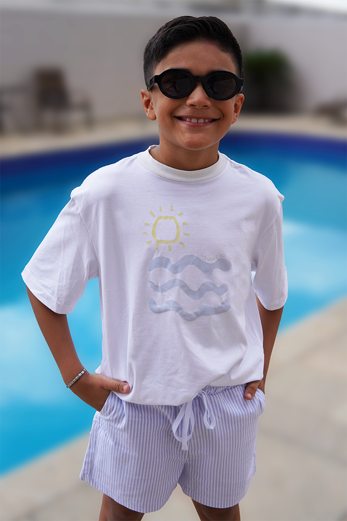 modelo usando look completo olivo kids, sendo camiseta estampada lá vem o sol e bermuda listrada