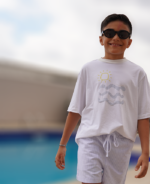 modelo vestindo camiseta olivo kids lá vem o sol e bermuda listras azuis